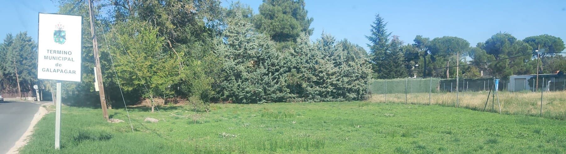 Finca de hierba junto a la carretera, con el cartel del término municipal de Galapagar a la izquierda