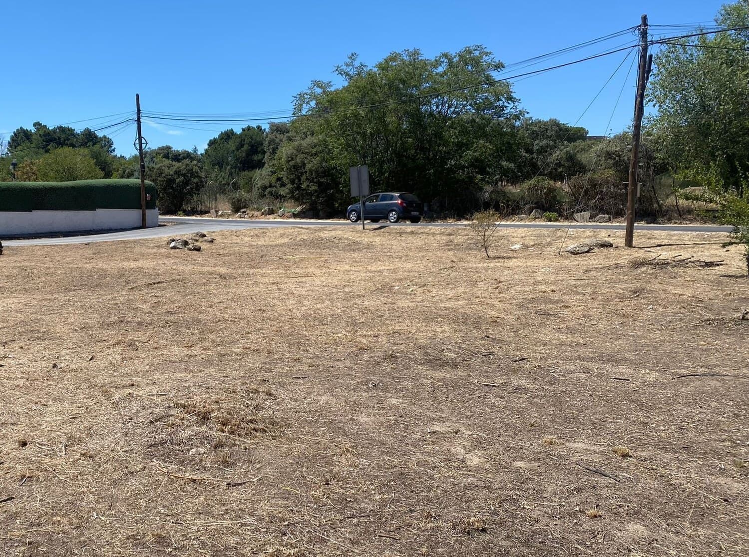 Solar urbano sin edificar, con el terreno seco y arbolado al fondo, antes de un levantamiento
